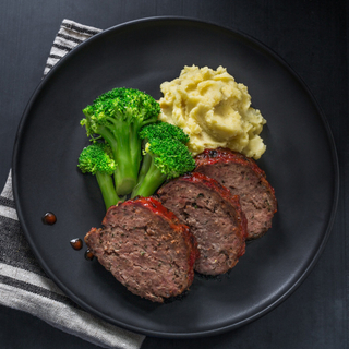 black plate with three slices of classic meatloaf, three broccoli spears and mashed potateos