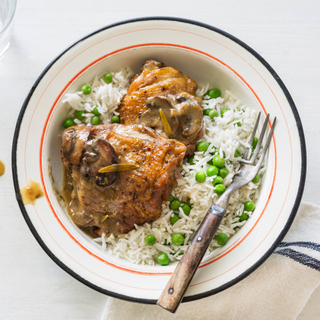 White bowl of mushroom braised skin-on chicken thighs with rice and green peas