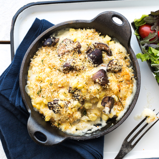 Mushroom corn macaroni and cheese in a cast iron pan on a white enameled tray with a side salad of greens and tomatoes. 