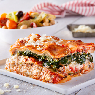 slice of veggie lasagna on a white plate with an Italian salad in the background