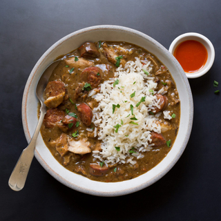 white bowl of Creole style gumbo with chicken and sausage with white rice and hot sauce