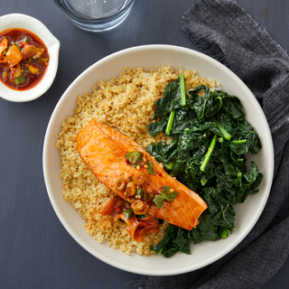 White dinner plate with quinoa, sauteed greens and pan-seared fillet of salmon with chunky pickled ginger dressing on top and in a dish on the side. 