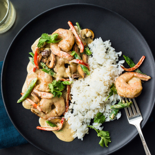 panang curry shrimp with white rice and vegetables in a black bowl
