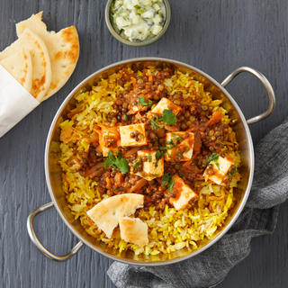 Paneer and lentil stew over a bed of basmati rice with folded naan on the side on a dark wooden table. 