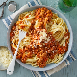 fettuccine pasta with bolognese sauce and shredded cheese in a round bowl with a fork on top