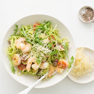 Bowl of pesto and shrimp pasta in a white bowl with side dishes of parmesan cheese and pepper 