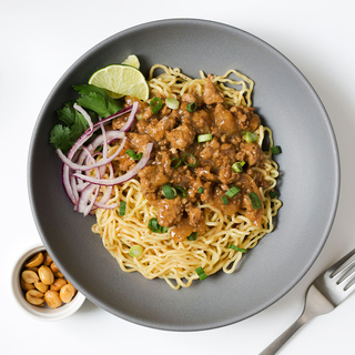 pork adobo over ramen noodles with fresh lime and red onion in a matte grey bowl on a white table