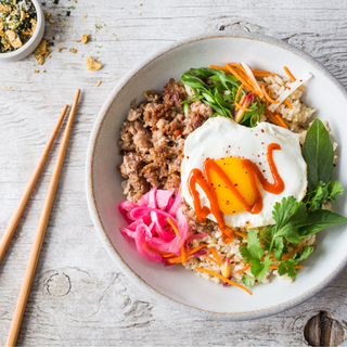 black bowl with vietnamese pork, rice, a fried egg and crunchy vegetables