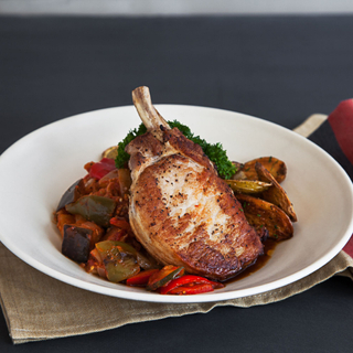 seared pork chop over ratatouille in a white dinner bowl