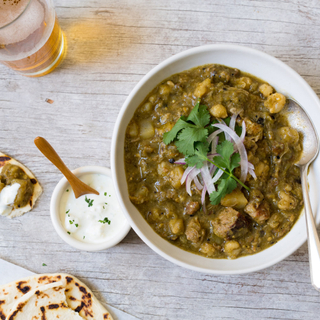 white bowl with chile verde and pork hominy stew with fresh cilantro and red onions on top