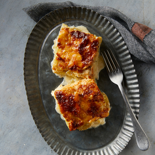 Two square slices of potato gratin with a browned top on a galvanized tin plate with a fork on the side. 