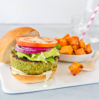 quinoa spnach burger on a toasted bun with lettuce, tomato and red onion with roasted sweet potato cubes in a bowl on the side