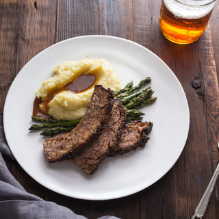 slices of red wine braised beef brisket with mashed potatoes and roasted asparagus on a white dinner plate