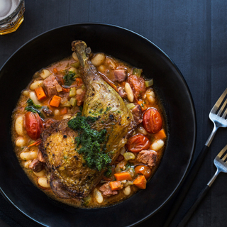 roasted chicken leg with cajun beans and tomatoes in a black bowl