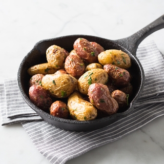 Cast iron pan with roasted garlic and parsley potatoes on a striped linen napkin