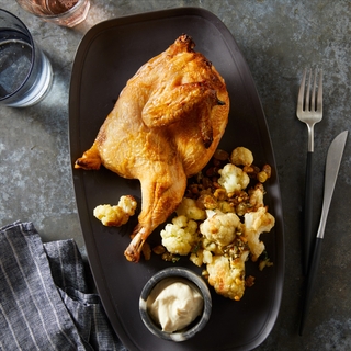 black long plate with half a roasted chicken and roasted cauliflower with anchovy aioli in a dish