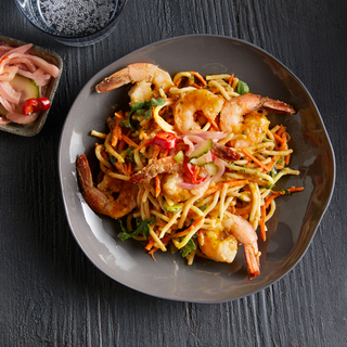 Brown round dinner plate with roasted shrimp and noodle salad. 