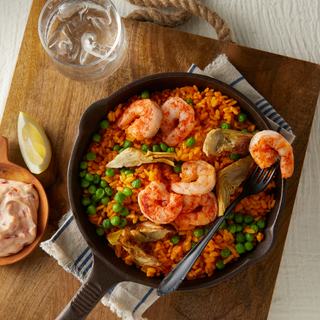 Cast iron skillet with saffron rice topped with roasted shrimp with a black fork on top on a wooden board on a wooden tabletop. 