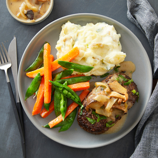 salisbury steak with mashed potatoes, steamed carrots and pea on a grey dinner plate