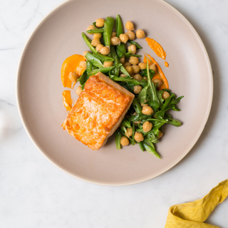 roasted salmon fillet with chickpea and arugula salad and romesco sauce on a white plate