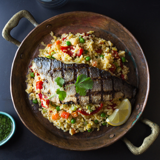 Copper pot filled with paella rice with a half branzino sea bass grilled and topped with fresh herbs. Served with a lime wedge and a dish of chimichurri sauce on the side. 