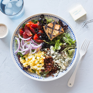 cobb salad with grilled salmon, onions, tomatoes, corn and lettuce in a bowl