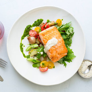 seared salmon fillet with mustard dressing, green and fresh raw vegetable salad on a white dinner plate