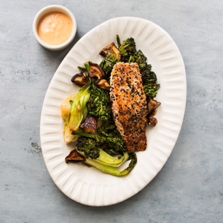 Large white platter with sesame seared salmon, sauteed greens and a side of dipping sauce on a grey concrete background