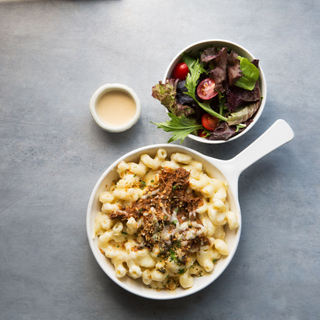 white pan with mac and cheese topped with short ribs with a side salad of greens and cherry tomatoes