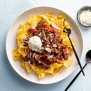pappardelle pasta with braised short rib sauce and grated cheese on a white dinner plate
