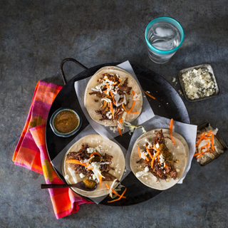 three shredded beef tacos on corn tortillas with carrot slaw and crumbled queso fresco on a black serving tray