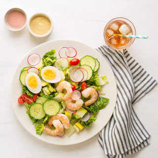 shrimp remoulade salad with green lettuce and hard boiled eggs on a dark round dinner plate