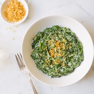 Round white bowl with creamed spinach, garnished with bread crumbs, on a marble surface