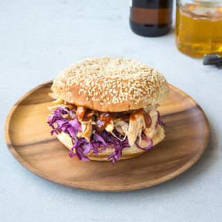 smoked pulled chicken sandwich on a potato bun with red cabbage slaw and barbecue sauce on a wooden dinner plate