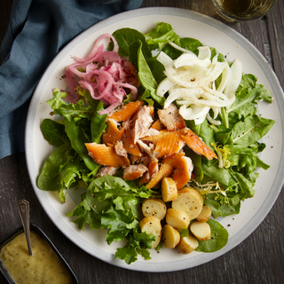 Salad with greens, pieces of smoked trout, steamed small potatoes, pickled red onions with salad dressing in a dish on the side. 