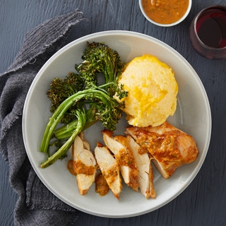 sliced southwestern spiced chicken breast with cheesy polenta and roasted broccolini in a white bowl