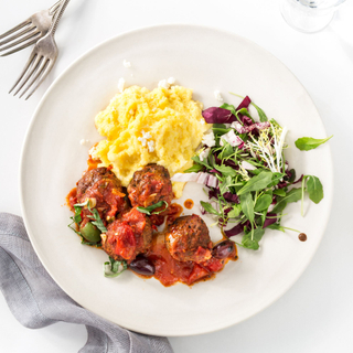 spiced lamb meatballs on a white plate with cheesy polenta and a green salad