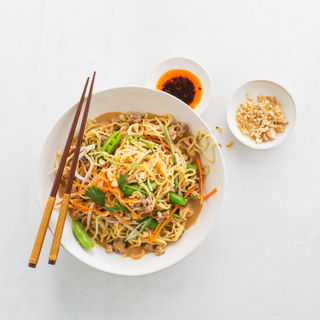 dan dan noodles with fresh vegetables and sauce in a white bowl and chopsticks