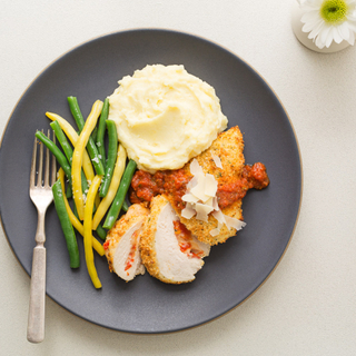 stuffed chicken parmesan with mashed potatoes and green and yellow beans on a black dinner plate