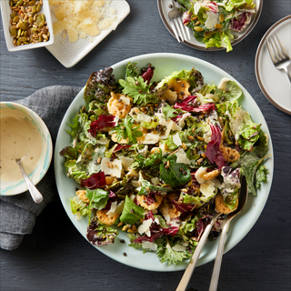 Super caesar salad with chopped lettuces on a teal plate with a fork and spoon int the salad and dressing on the side on a dark table with a small side late of more salad. 