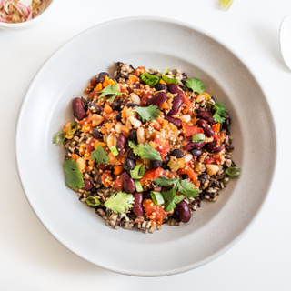 Super protein chili with rice, beans and vegetables topped with fresh cilantro in a round white bowl on a white table with a dish of sour cream and toppings on the side. 