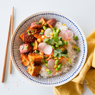 teriyaki yam bowl with white rice, roasted sweet potato, radishes, edamame and carrots in a blue and white bowl