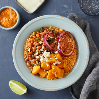 Tex-Mex veggie rice bowl with rice, poblano peppers, pinto beans and sliced red onions in a blue bowl with a sliced lime on the side on a dark blue background with a grey napkin. 