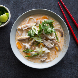 bowl of thai chicken curry soup with rice noodles, fresh herbs and colorful vegetables