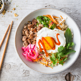 thai pork bowl with a fried egg, ground pork and brown rice in a white bowl with chopsticks