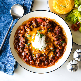 bowl of three bean chili with sour cream, cheese and sliced scallions 