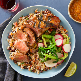 seared asada tri-tip steak over rice with cooked and raw vegetables in a blue bowl