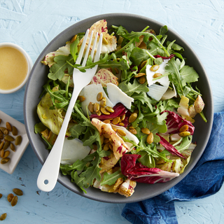 Tricolore salad with greens, radicchio and endive in a blue round bowl on a bright blue background with a blue napkin and a white fork on top 