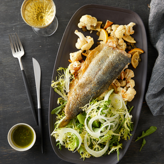 grilled trout with brown butter cauliflower and green salad on a black long plate with a glass of wine