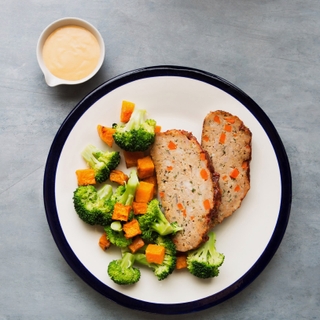 two slices of turkey meatloaf with broccoli and butternut squash on a white dinner plate with a side of sauce